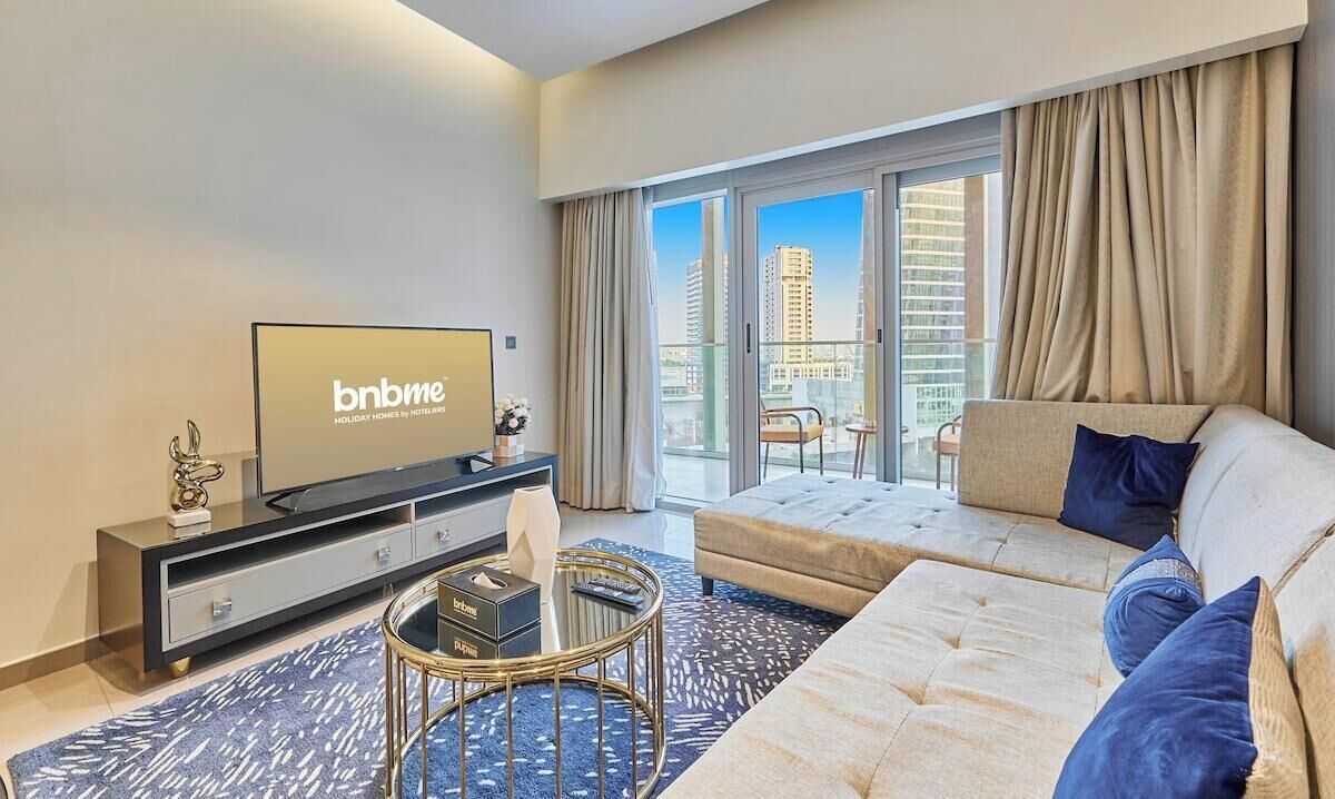 Una habitación de hotel moderna con un ventanal grande, un sofá, un televisor y una mesita redonda.