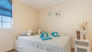 A bedroom with a bed, a nightstand, a window with blinds, and wall art. - Casa Bella 1 - Apartment with Sea and Beach Views (Costa Calma)
