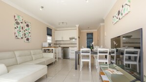 A modern living room with a white sofa, a dining area with a glass table, and a kitchen in the background. - Casa Bella 1 - Apartment with Sea and Beach Views (Costa Calma)