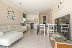 A modern living room with a white sofa, a dining area with a glass table, and a kitchen in the background. - Casa Bella 1 - Apartment with Sea and Beach Views (Costa Calma)