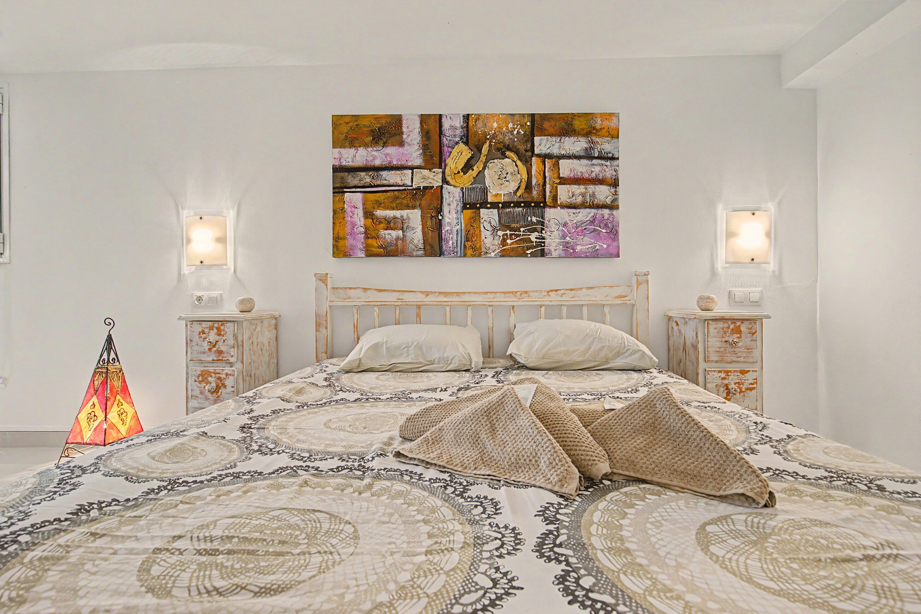 A bedroom with a bed, two bedside tables, a wall-mounted artwork, and a decorative floor lamp.