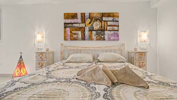 A bedroom with a bed, two bedside tables, a wall-mounted artwork, and a decorative floor lamp.
