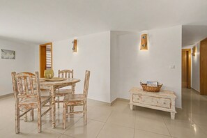 Un coin repas avec une table ronde et des chaises, une petite table d’appoint avec un panier, et une porte donnant sur une autre pièce.