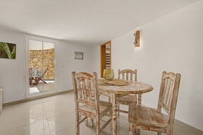 A dining area with a round table and four chairs, a glass door leading outside, and a wall-mounted light fixture. - Casa Bella 2 – 100 m² Apartment for Four Guests, 3 Minutes from the Beach (Costa Calma)