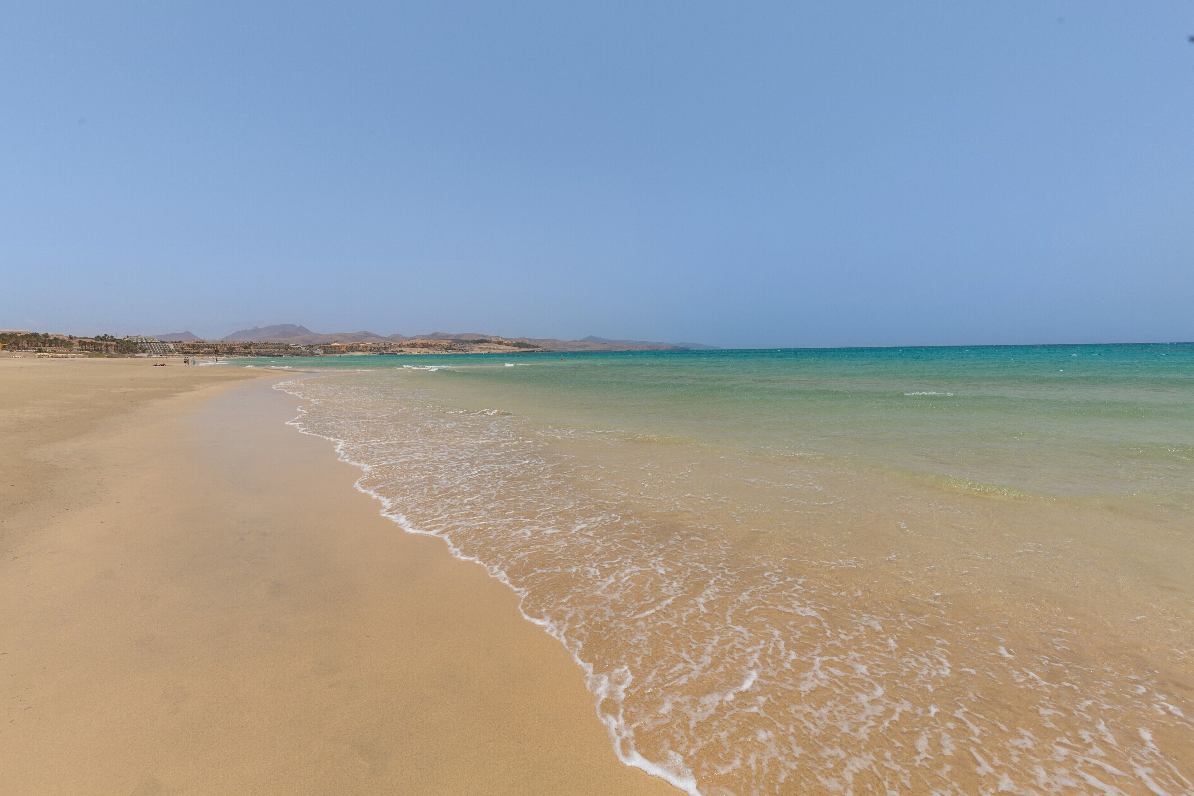 A beach with clear water, a sandy shore, and distant mountains.