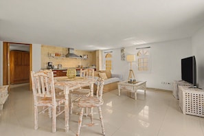 A spacious living area with a dining table, chairs, a sofa, a television, and a kitchen in the background. - Casa Bella 2 – 100 m² Apartment for Four Guests, 3 Minutes from the Beach (Costa Calma)