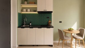 A compact kitchen with a black countertop, a sink, and a dining area with a round table and two chairs. - Centraltique Passage Living (Hanoi)