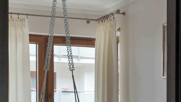 A room with a hanging chair, a round rug, a wooden door, and a window with curtains. - Spacious Apartment with a Balcony | Parking | 2 Bedrooms (Toruń)