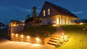 Una casa moderna con un vialetto in pietra che conduce all'ingresso, un pontile in legno e un'area prato ben illuminata.