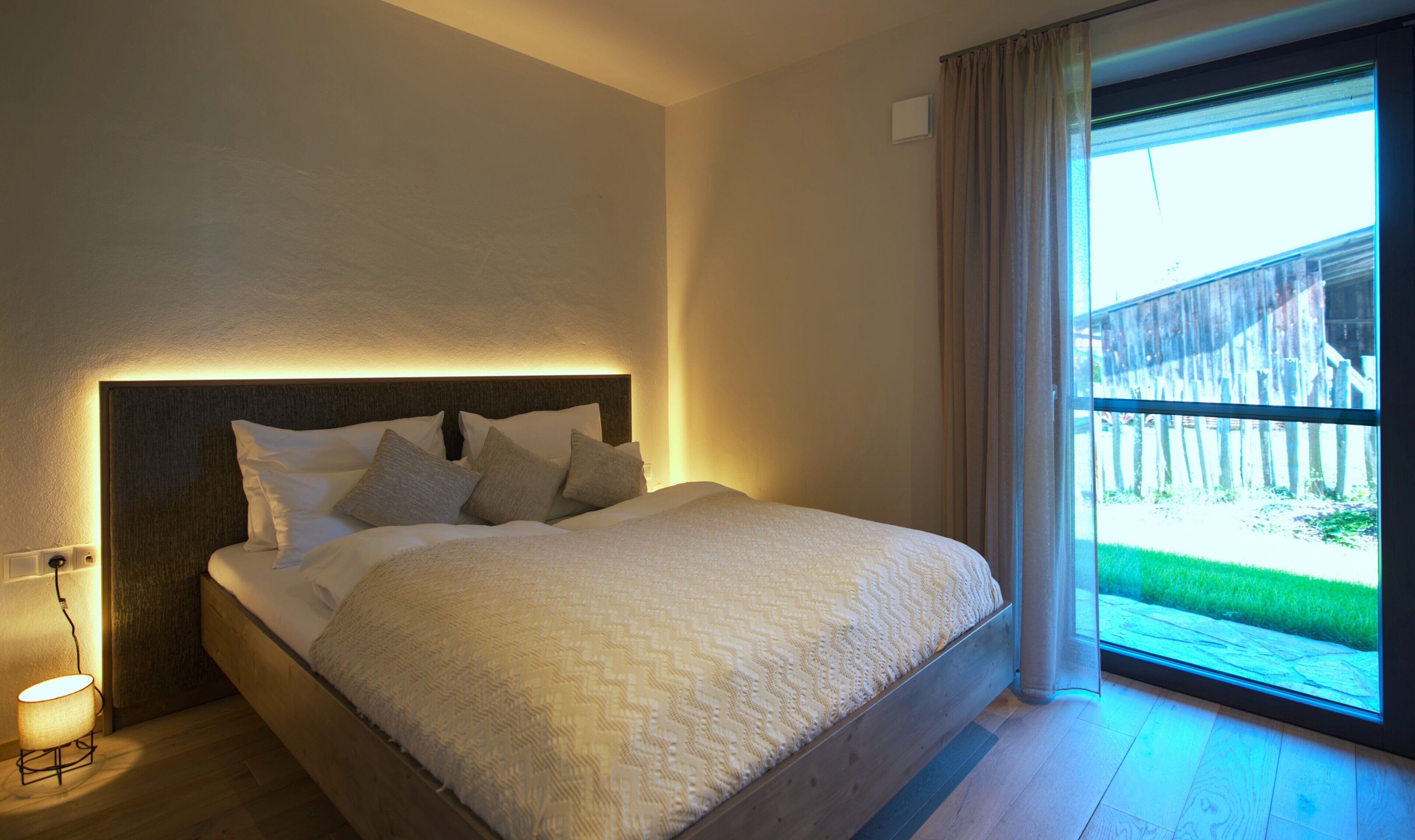 Un dormitorio con cama, lámpara de noche y ventana con cortinas.