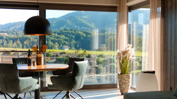 Un'area pranzo moderna con tavolo, sedie e vista su un paesaggio montuoso attraverso ampie finestre.