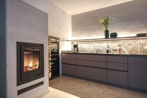 A modern kitchen with a built-in fireplace, marble countertop, and a vase with flowers on the shelf. - Stunning view | 2 bathrooms, 2 toilets, fireplace, electric charging station (Bischofegg)