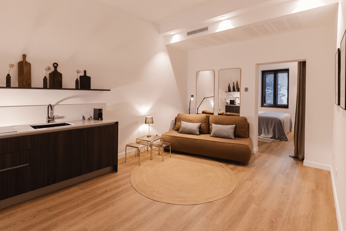 A modern kitchen with a built-in sink, a round dining table, and a sofa in the living area.