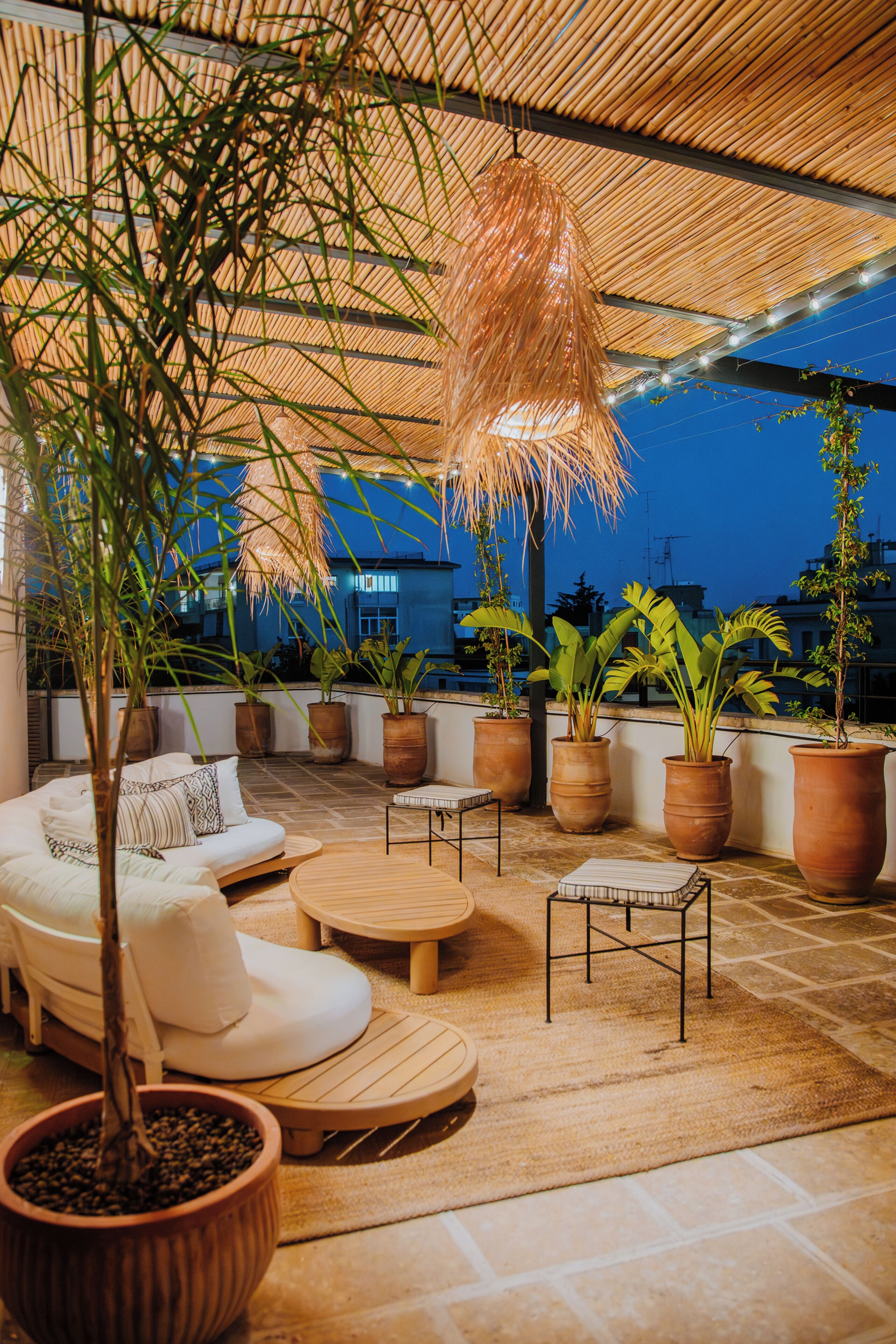 An outdoor seating area with a thatched ceiling, potted plants, and a white sofa.