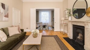 A living room with a sofa, coffee table, fireplace, and a view into another room. - The Steele Blue House (London)