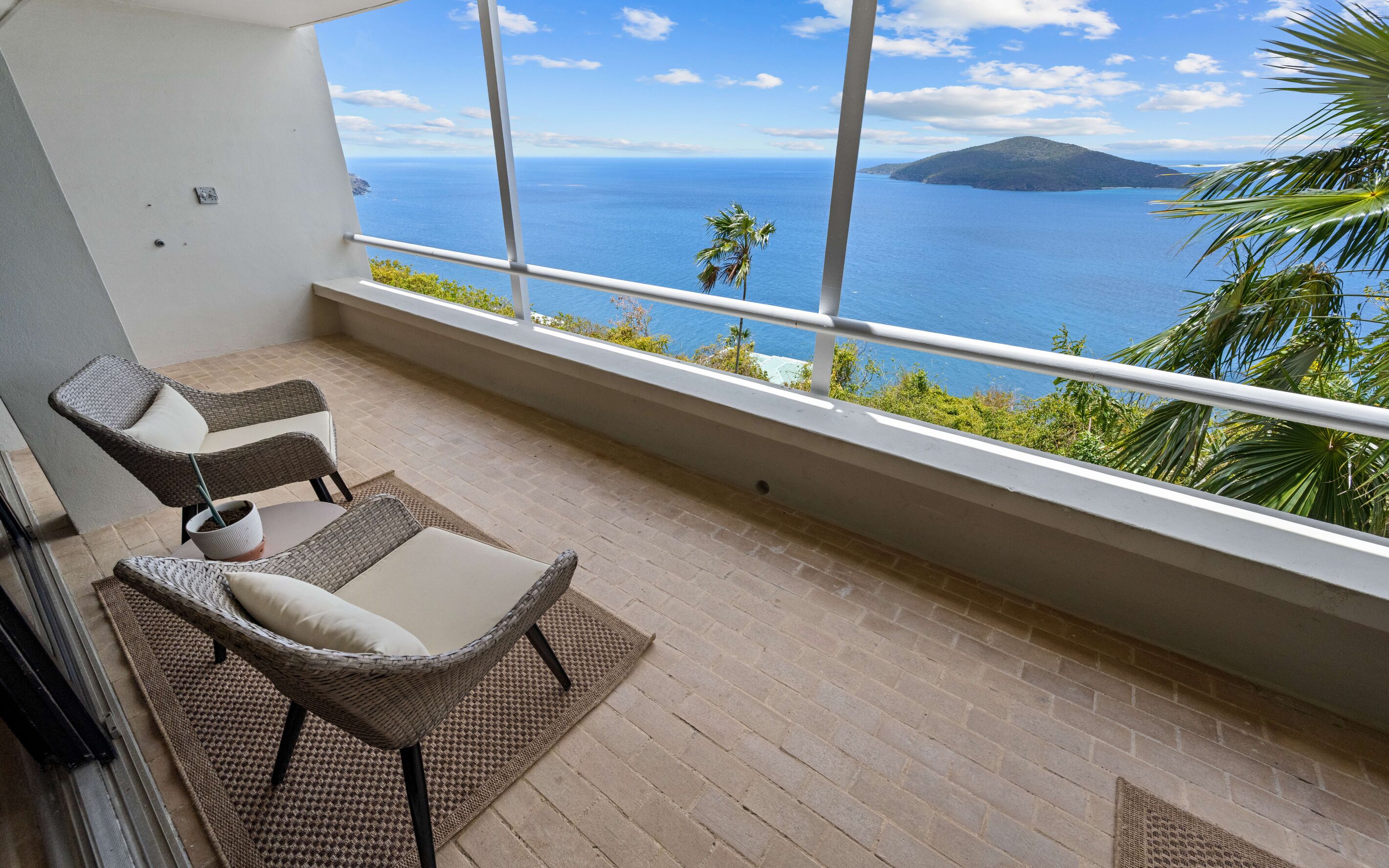 Un balcon avec des fauteuils en osier et une petite table, offrant une vue sur la côte, avec une montagne et la mer en toile de fond.