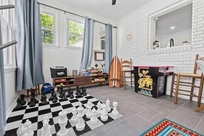 A room with a large checkered chessboard, a Nintendo Switch, and a small table with a colorful design. - The Tranquil Token-hot Tub & Ping Pong Table (North Charleston)