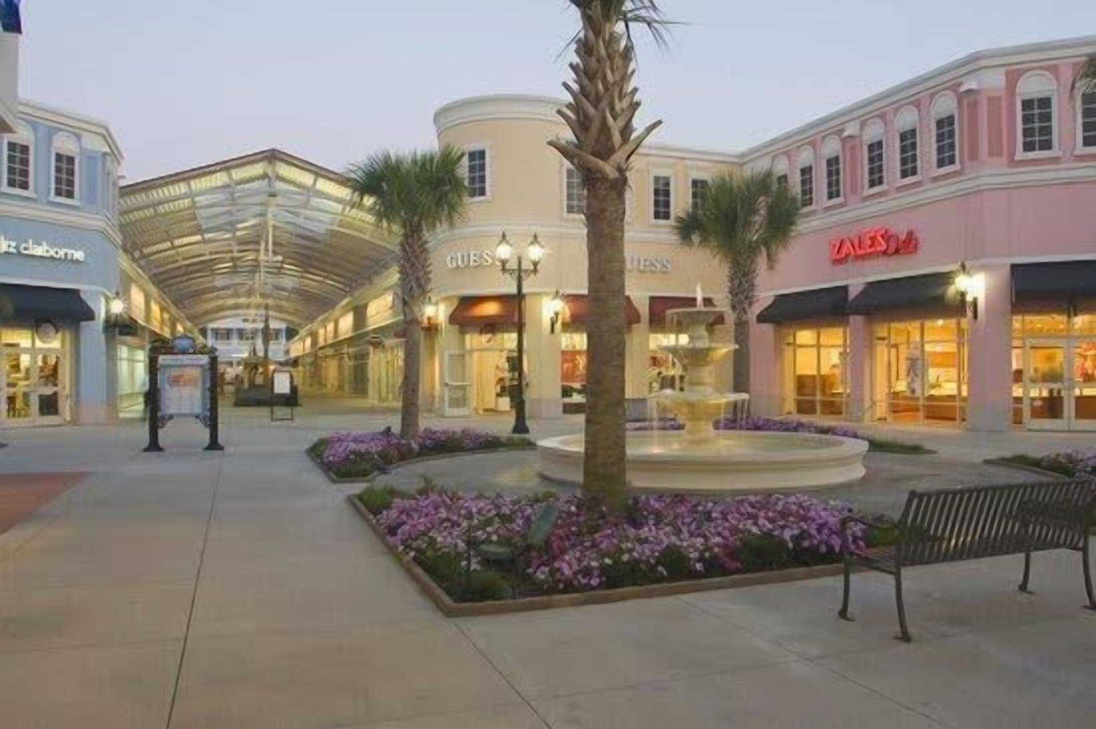 A shopping mall with a central fountain, palm trees, and benches.