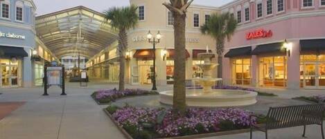 A shopping mall with a central fountain, palm trees, and benches.