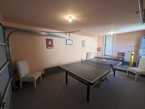 A room with a ping pong table, two chairs, a small table, and a door. - The Tranquil Token-hot Tub & Ping Pong Table (North Charleston)