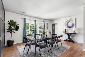A dining area with a glass table, black chairs, a potted plant, and a view through large windows. - The Tranquil Token-hot Tub & Ping Pong Table (North Charleston)
