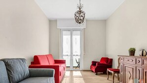 Un soggiorno con un divano grigio, poltrone rosse, un mobile in legno e un lampadario.