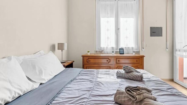 Una camera d'albergo con un letto, una cassettiera in legno, un comodino e una finestra con tende.