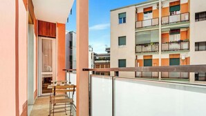 Un balcone con una sedia e un tavolo in metallo, una porta scorrevole e vista su un edificio a più piani con balconi.