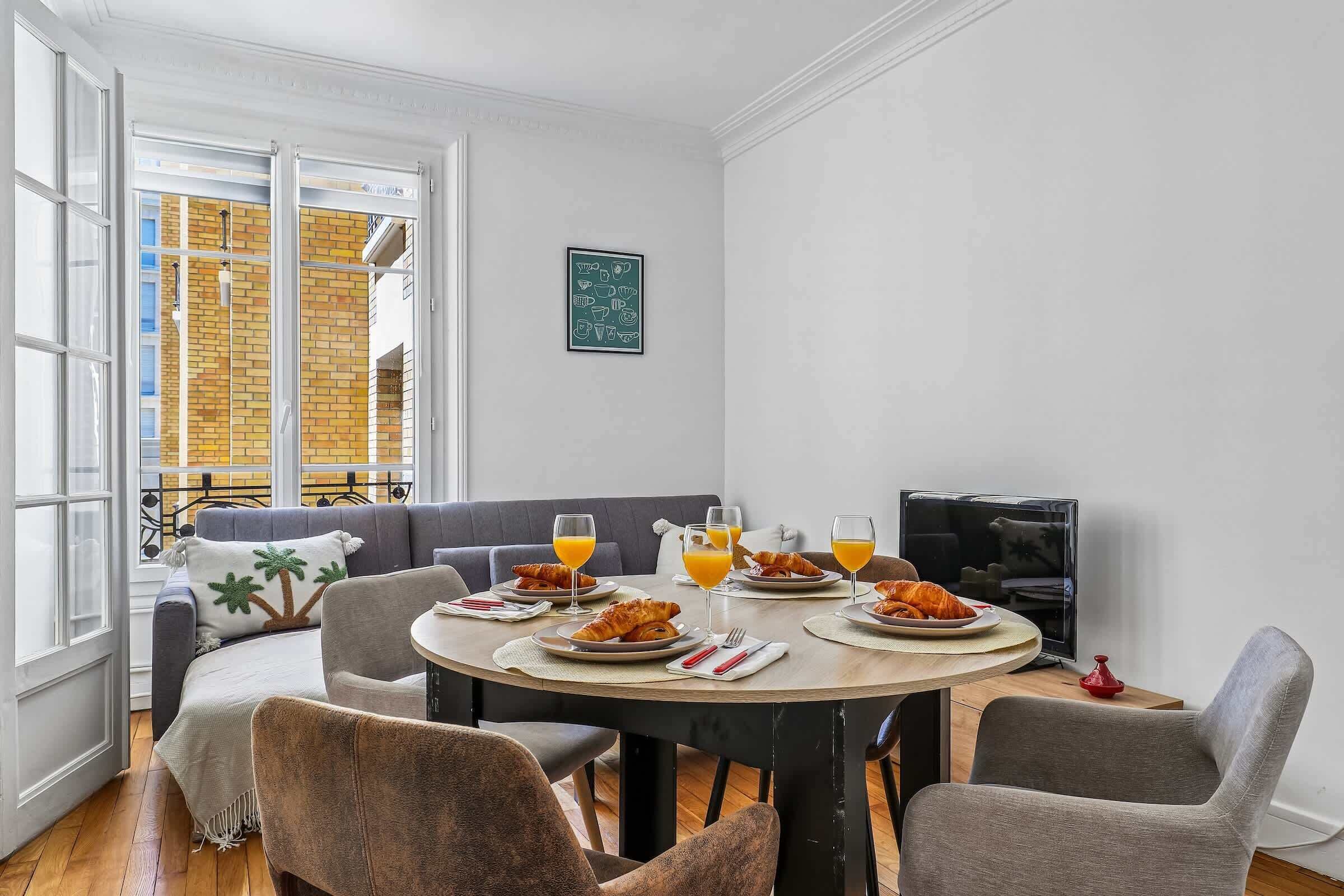 Un comedor con una mesa redonda, sillas grises, un sofá y un televisor.