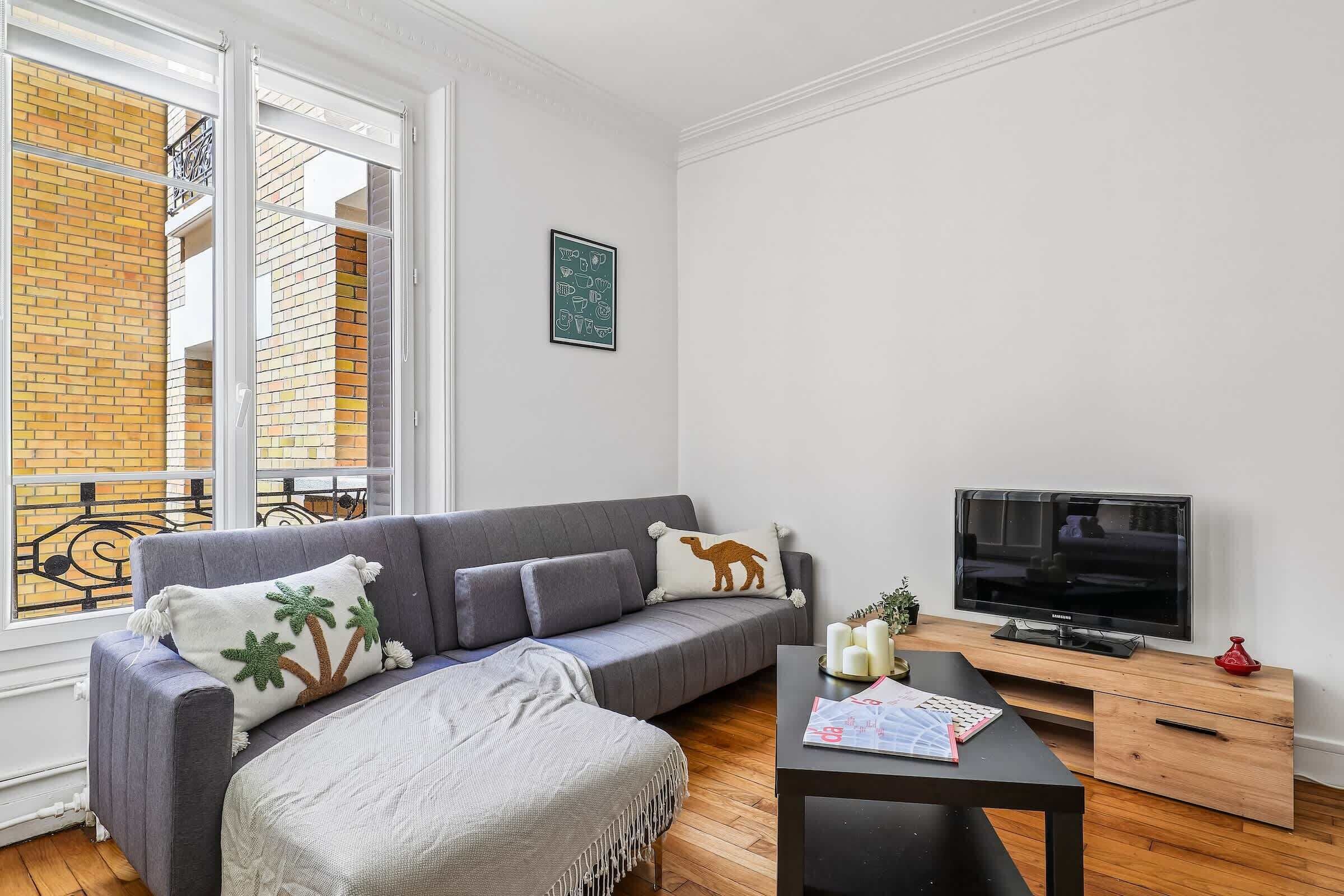 Un salon moderne avec un canapé gris, un téléviseur et une table basse en bois.