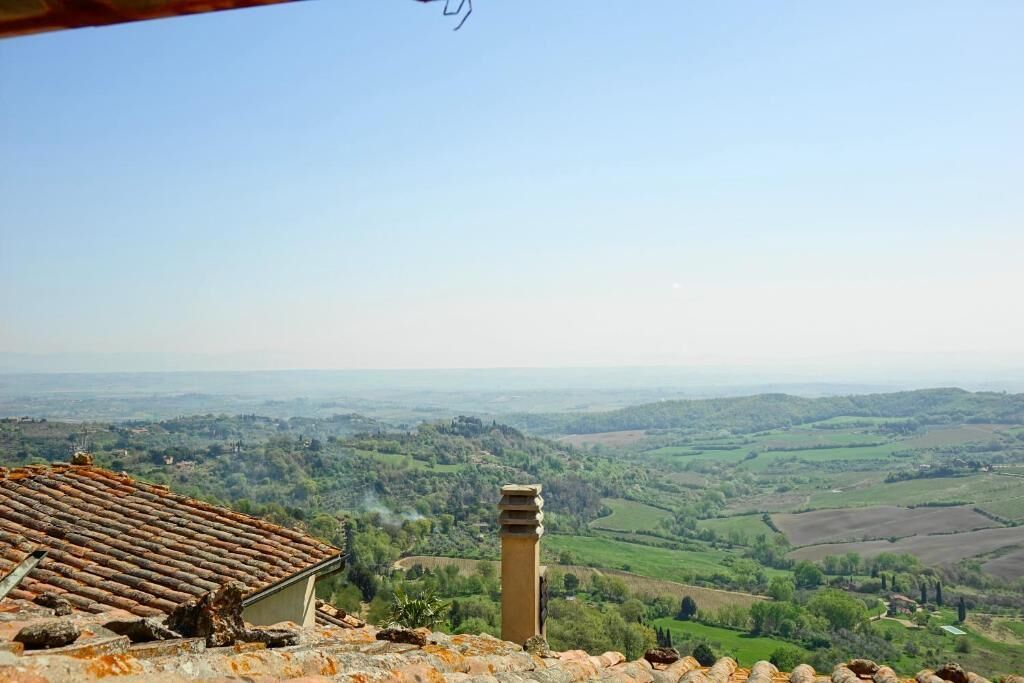 A view from a building with a tiled roof overlooking a valley with fields and distant hills.