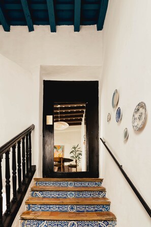 A staircase with blue and white patterned tiles leading to a room with a wooden ceiling and a hanging light fixture. - Casa Torno - El Mirador (Sanlúcar de Barrameda)