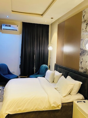 Habitació d'hotel amb llit, escriptori, cadira, aire condicionat i un llum penjada a la paret.