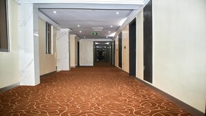 Un pasillo de hotel con alfombra estampada, paredes de mármol y puertas que dan a habitaciones.