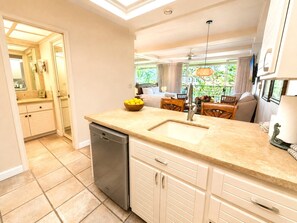 A modern kitchen with a dishwasher, a sink, and a dining area with a table and chairs. - Whaler | Ocean View Studio | Kaanapali Beach | Car Incl. w/ 6+ Nights | WH2-465 by KBM (Lahaina)