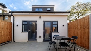 A modern house with two black-framed windows, a wooden fence, and a patio with a table and chairs. - Greenford Apartments (Wembley)