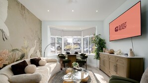 A modern living room with a sofa, a coffee table, and a TV mounted on the wall. - Greenford Apartments (Wembley)
