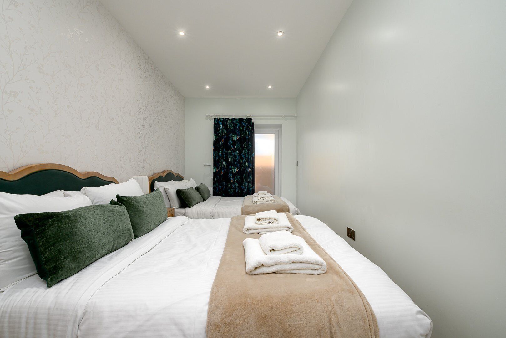 A hotel room with two beds, a wooden headboard, a window with curtains, and a door leading outside.