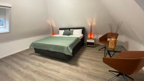 Un dormitorio con cama, mesitas de noche, una silla y una ventana.
