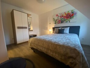 Un dormitorio con cama, armario, mesita de noche y un cuadro en la pared.