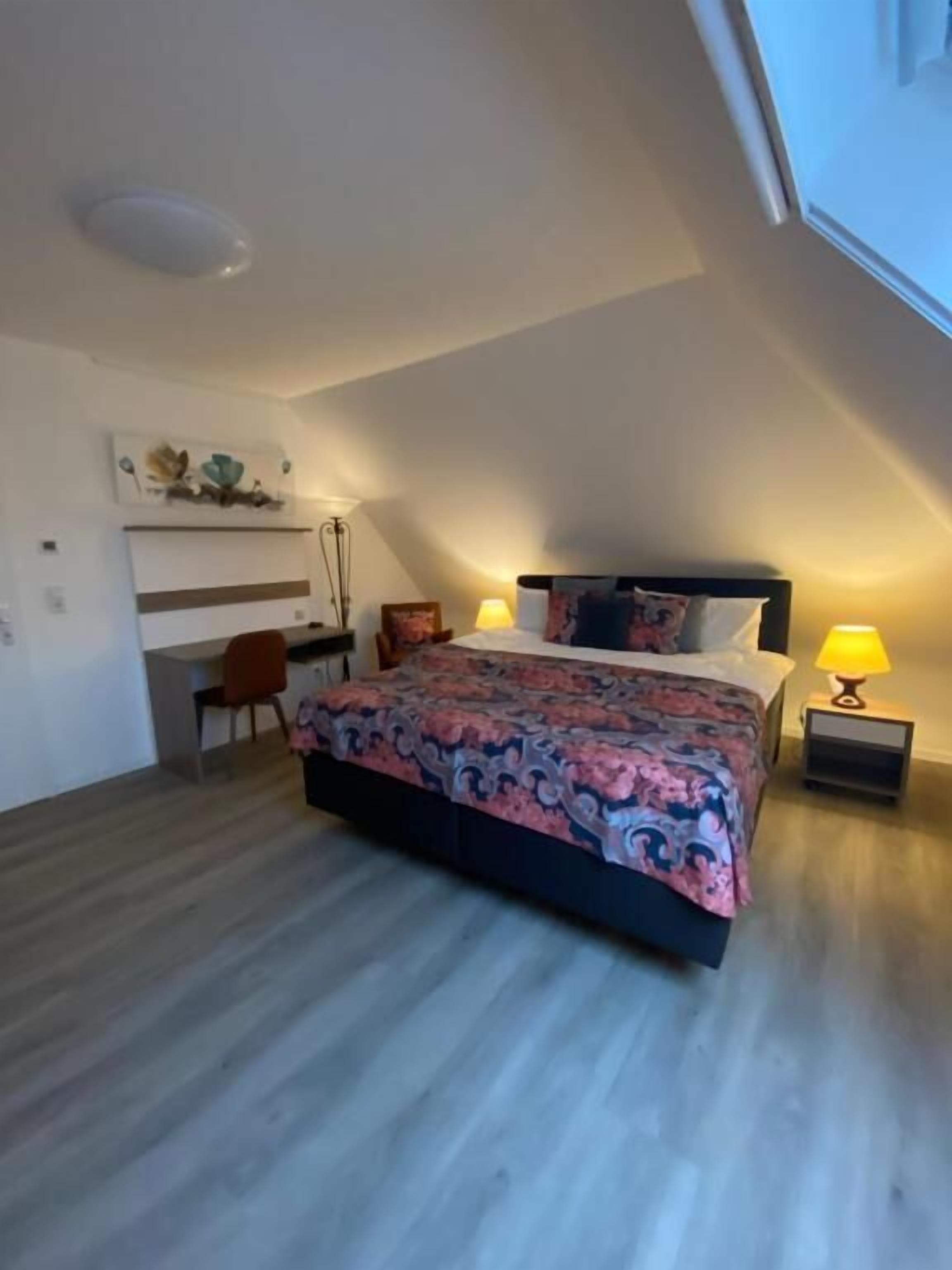 A bedroom with a bed, bedside tables, and a desk.
