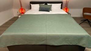 Una cama con una colcha verde, dos lámparas de noche y una silla en una habitación con techo inclinado.