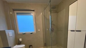 Un baño con cabina de ducha de vidrio, un inodoro y una ventana.