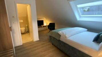 Une chambre à coucher avec un lit, une lucarne, un plancher en bois et une porte donnant sur une salle de bain.