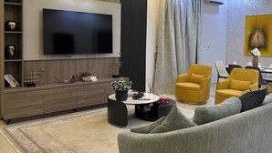 A modern living room with a flat-screen TV, a sofa, yellow armchairs, a coffee table, and a decorative plant. - D'CROWN PLACE (Abuja)