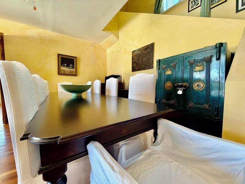 A room with a wooden table, white chairs, a green cabinet, and artwork on the walls.