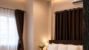 Habitación de hotel con una cama grande, una mesita de noche con lámpara, una ventana con cortinas y un equipo de aire acondicionado.