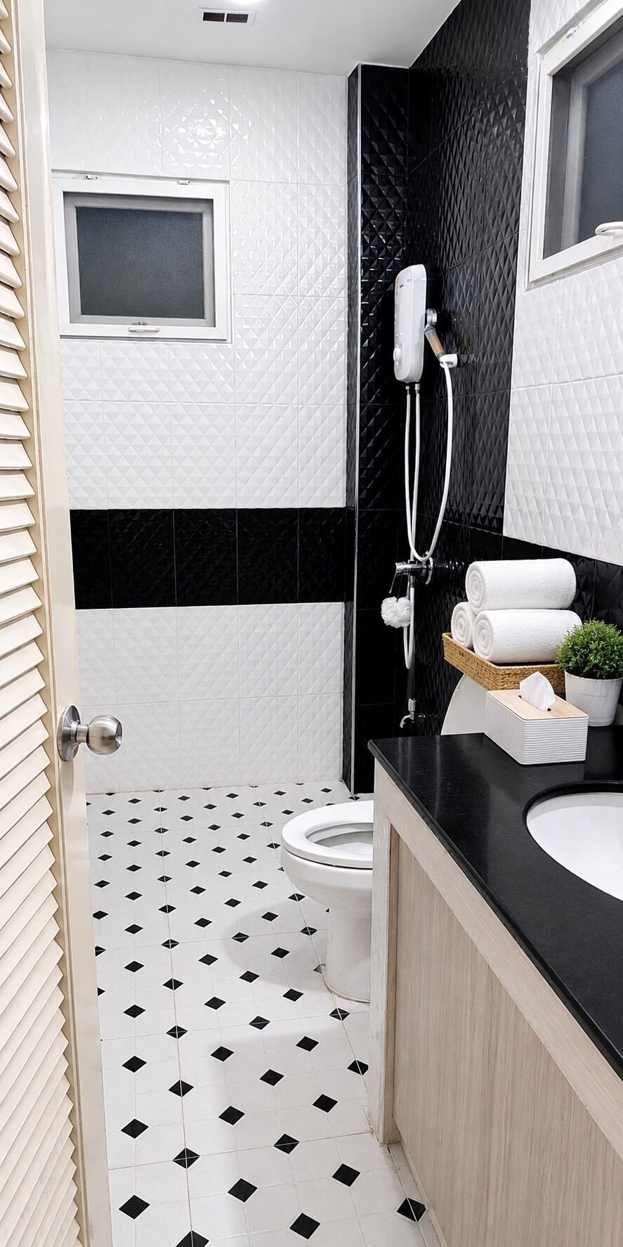 Een moderne badkamer met een zwart-wit betegelde vloer, een wit toilet, een zwart aanrecht met een wastafel en een douchegedeelte.