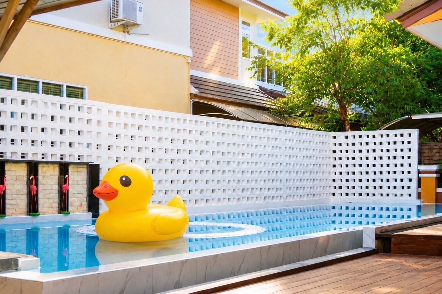 A swimming pool with a large inflatable duck, a white lattice fence, and a building with a sloped roof in the background.