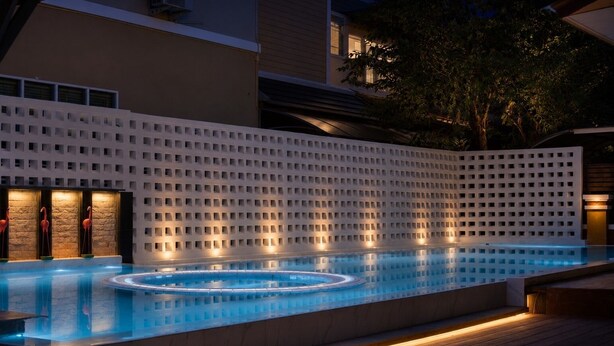 Una piscina con un diseño geométrico en la pared, una terraza de madera y un ambiente nocturno.
